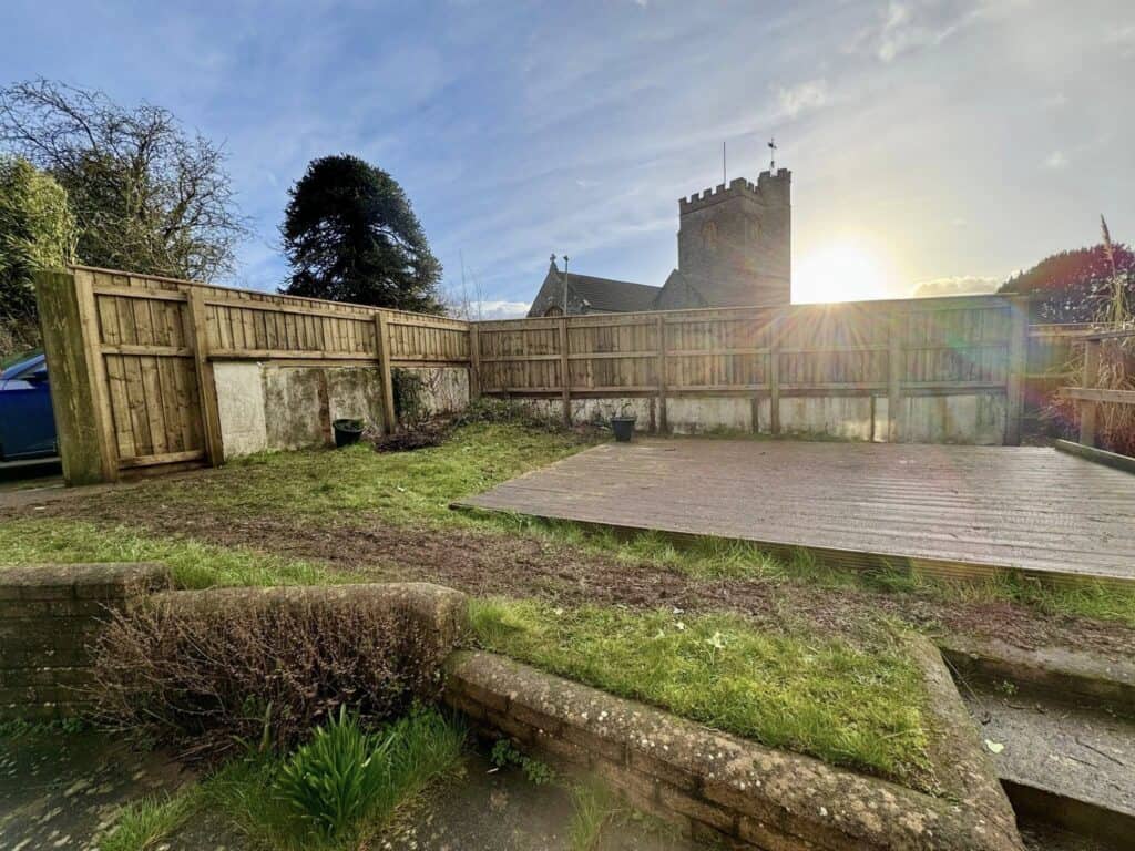 Backyard garden with wooden deck and church tower in background at sunset.