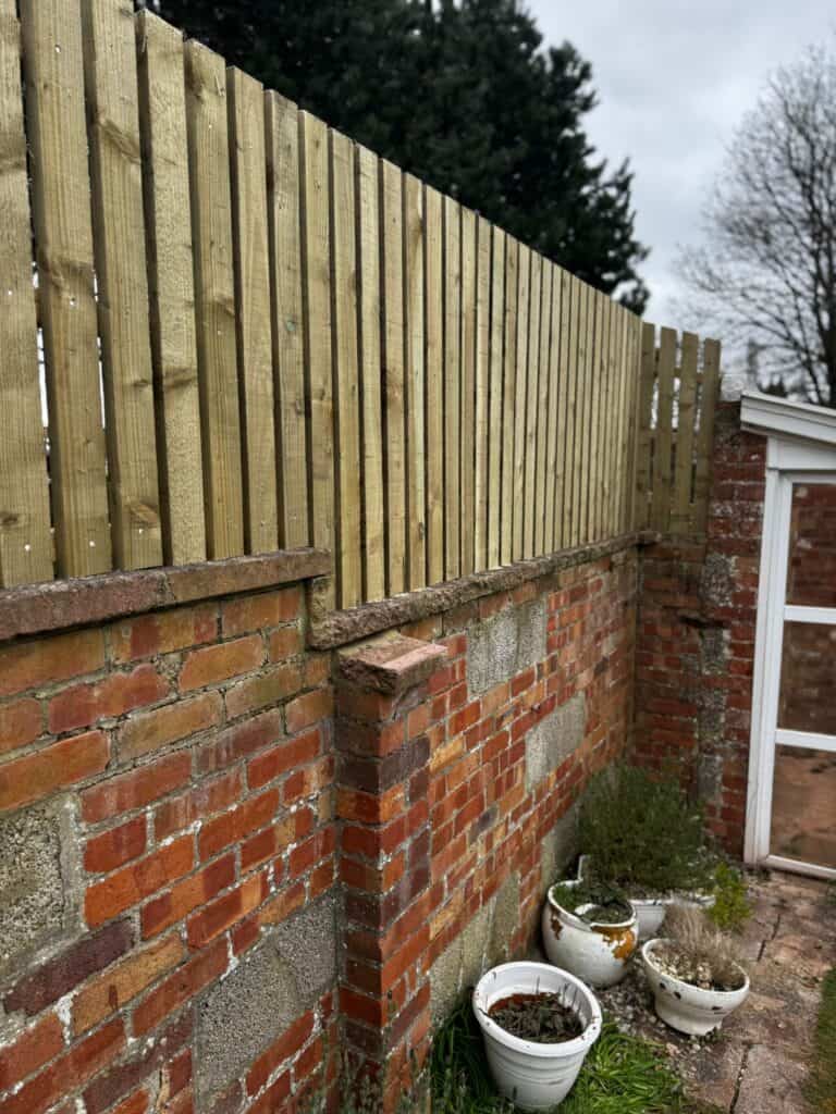 New wooden garden fence installed over brick wall in Devon.