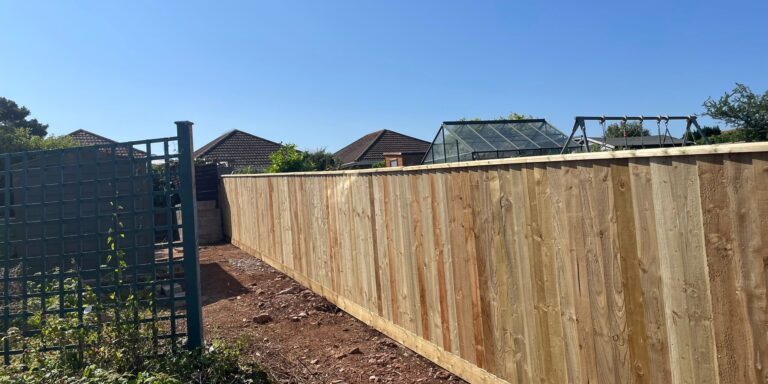 New wooden garden fence installed in a residential backyard under clear blue sky.