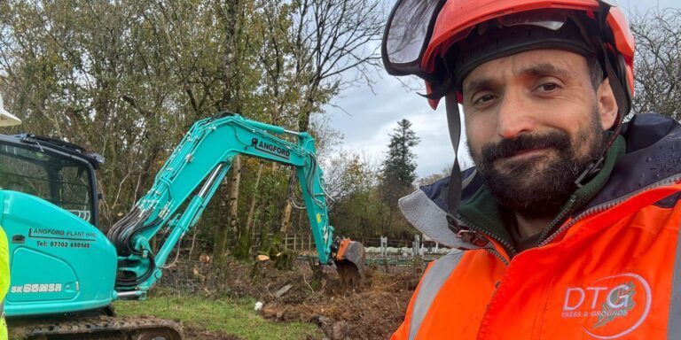 Devon Trees & Grounds worker in safety gear operating excavator.