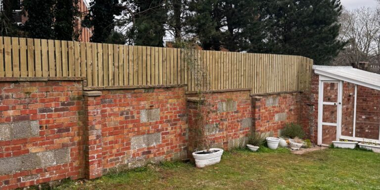Garden with brick wall, wooden fence, and greenhouse in Devon, UK.