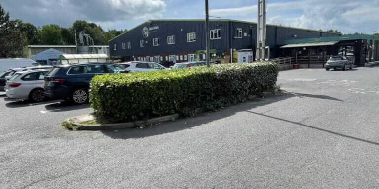 Car park outside Devon Trees & Grounds Ltd with hedges and parked vehicles.