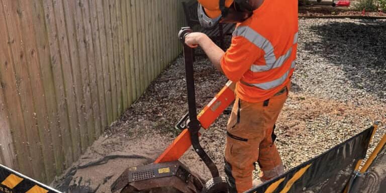 Tree surgeon using stump grinder near wooden fence in Devon.
