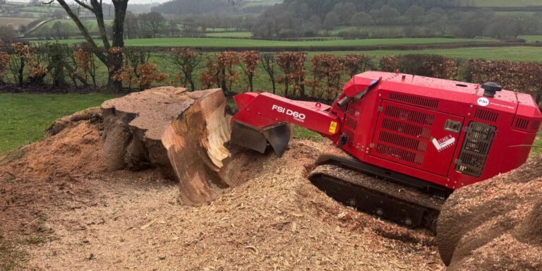 Red mini excavator chopping large rocks in a rural landscape.